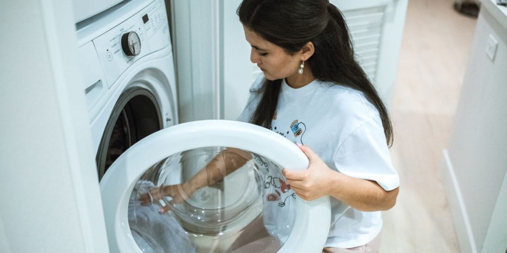 Gros plan de mains chargeant du linge dans un lave linge à hublot