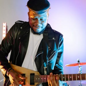Buneri.fr | Pourquoi les PDG de la tech et les rock stars vivent en veste en cuir Guitariste jouant de la guitare électrique sur scène avec des lumières vives, portant une veste en cuir et une casquette plate