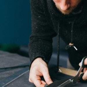 Serious male tailor with scissors cutting circle out of leather material while standing at workbench in atelier