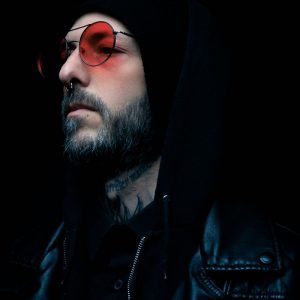 Portrait mélancolique d'un homme en veste de cuir noire et lunettes teintées rouges sur fond sombre
