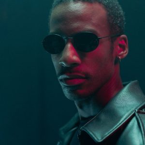 Buneri.fr | Une veste en cuir véritable vaut-elle vraiment son prix ? Portrait stylisé d'un homme en lunettes de soleil et veste en cuir dans une ambiance dramatique