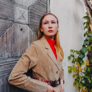 Buneri.fr | Les vestes en cuir dans les annees 1960, 1970 et 1980 Femme en veste de daim fauve appuyee contre une vieille porte patinee dans la lumiere d automne