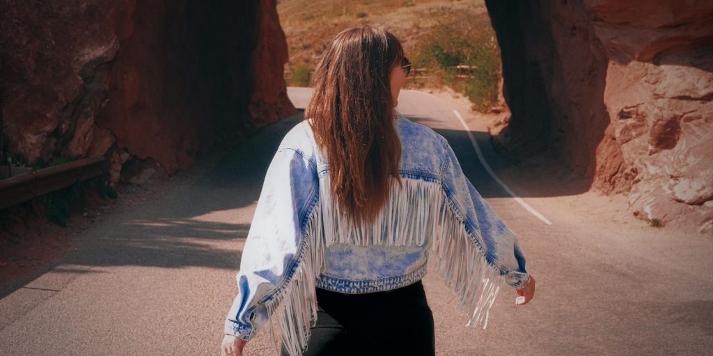Femme en veste à franges marchant dans un tunnel de pierre pittoresque par une journée d'automne ensoleillée