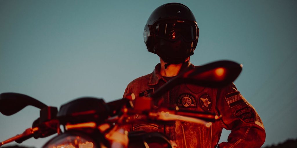 Un motard en casque et blouson de cuir pose près de sa moto au crépuscule