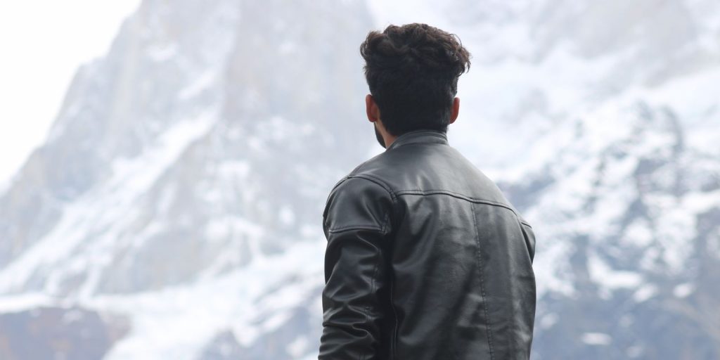 Un homme en veste de cuir contemplant des montagnes enneigées sous un ciel d'hiver dégagé