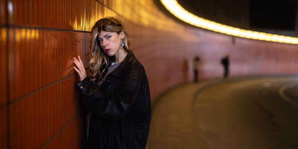 Une femme en veste en cuir pose contre un mur de tunnel illuminé, une ambiance urbaine
